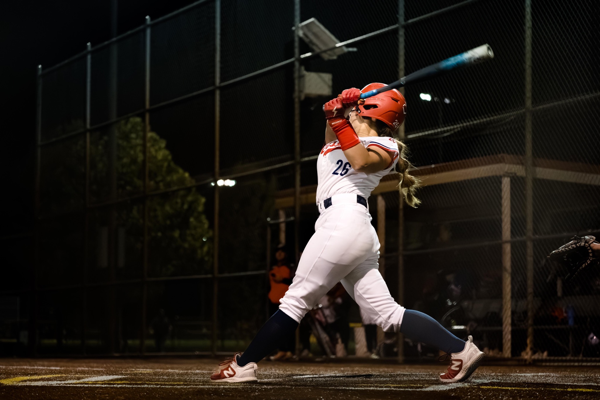 Mission softball player completing a powerful swing under the lights